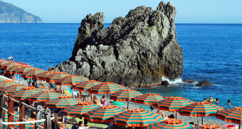 Vista della spiaggia di Monterosso al Mare con il mare sullo sfondo, uno scoglio e tanti ombrelloni aperti