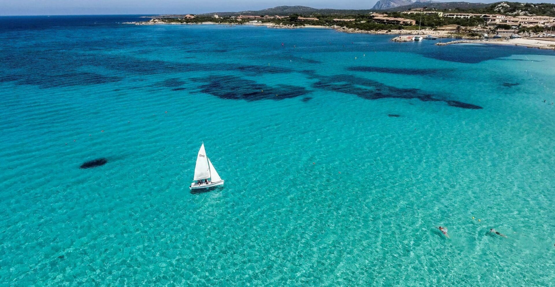 Barca a vela bianca che naviga nel mare della Sardegna con sfumature di blu e azzurro