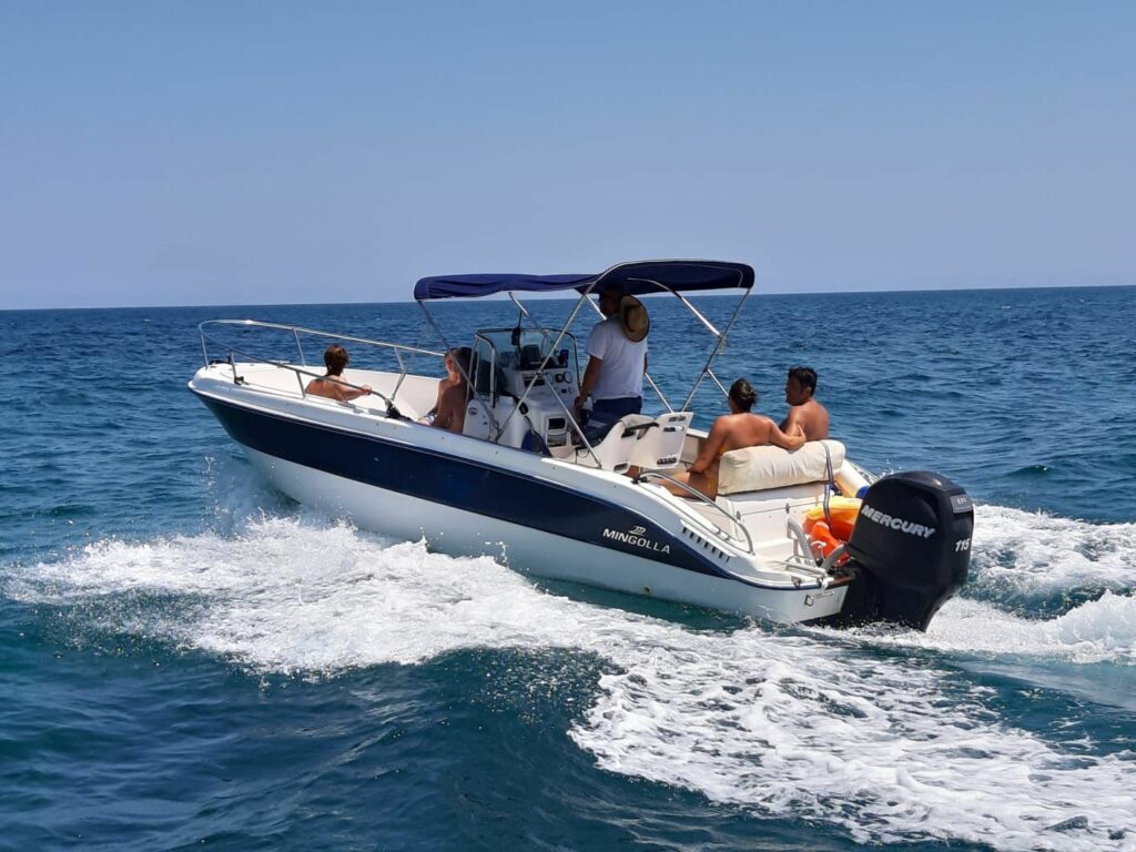 Persone a bordo di una barca a motore bianca con tendalino blu che sfreccia nel mare del Salento