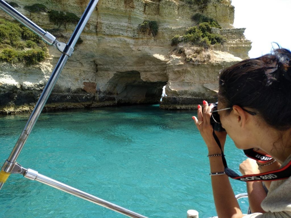Donna scatta una fotografia a bordo di una barca a una grotta del Salento con mare turchese