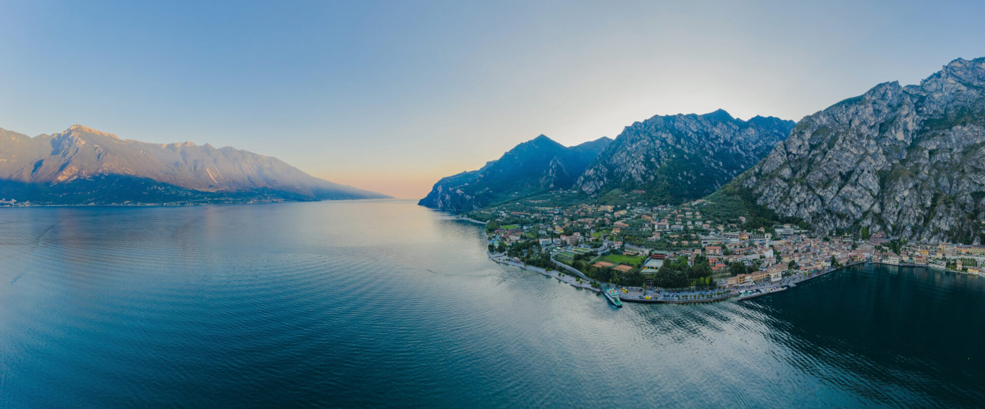 Veduta panoramica di Limone sul Garda al tramonto, con le montagne sullo sfondo e il lago che riflette la luce dorata, perfetta rappresentazione delle esperienze sul Lago di Garda tra natura, sport e benessere.
