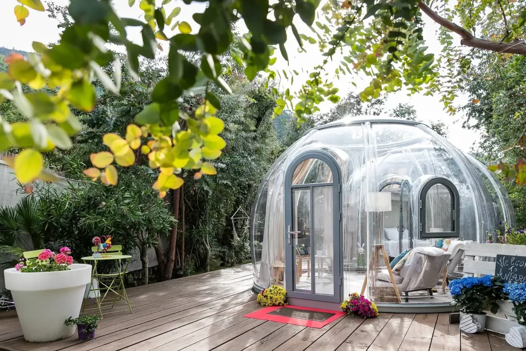 Bubble room trasparente in giardino, cupola panoramica tra alberi e vegetazione mediterranea