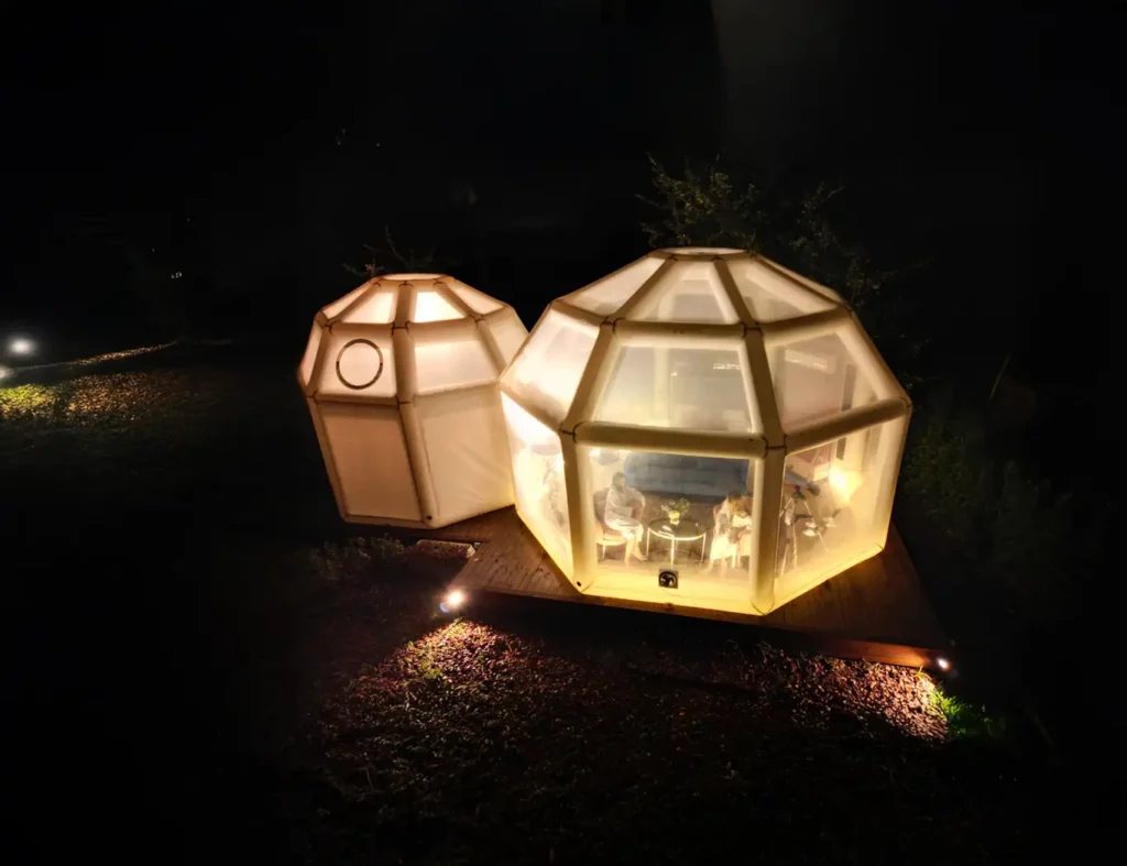 Bubble room illuminata di notte in Sicilia, cupola geodetica con interni visibili su pedana in legno