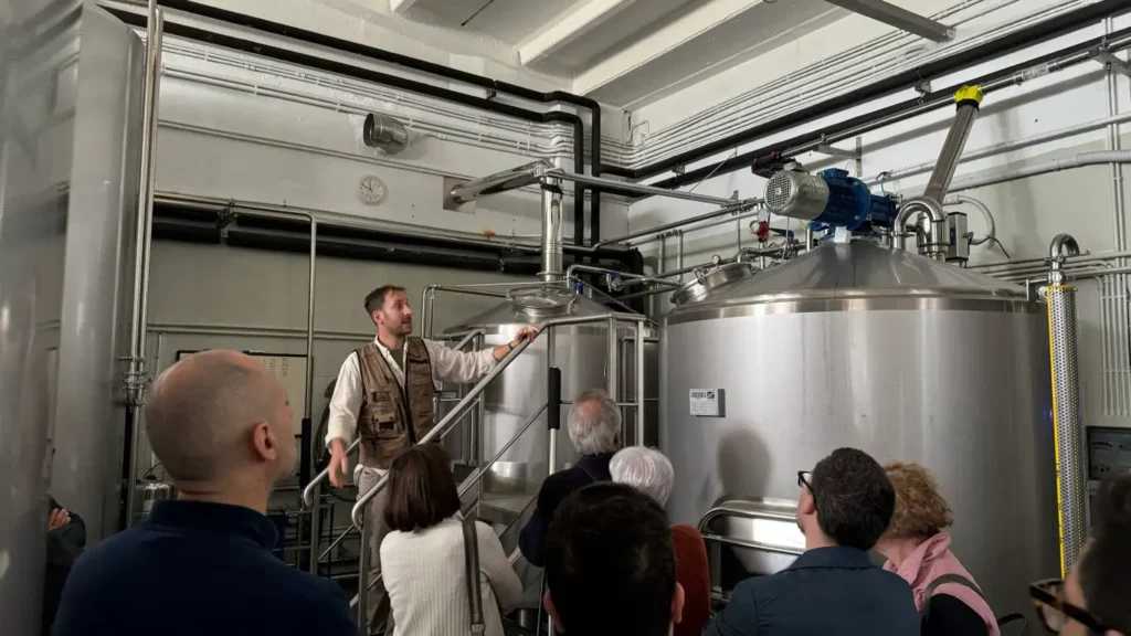 Visita guidata in birrificio in Lombardia con gruppo di partecipanti davanti a serbatoi di produzione, ideale per una degustazione di birra.