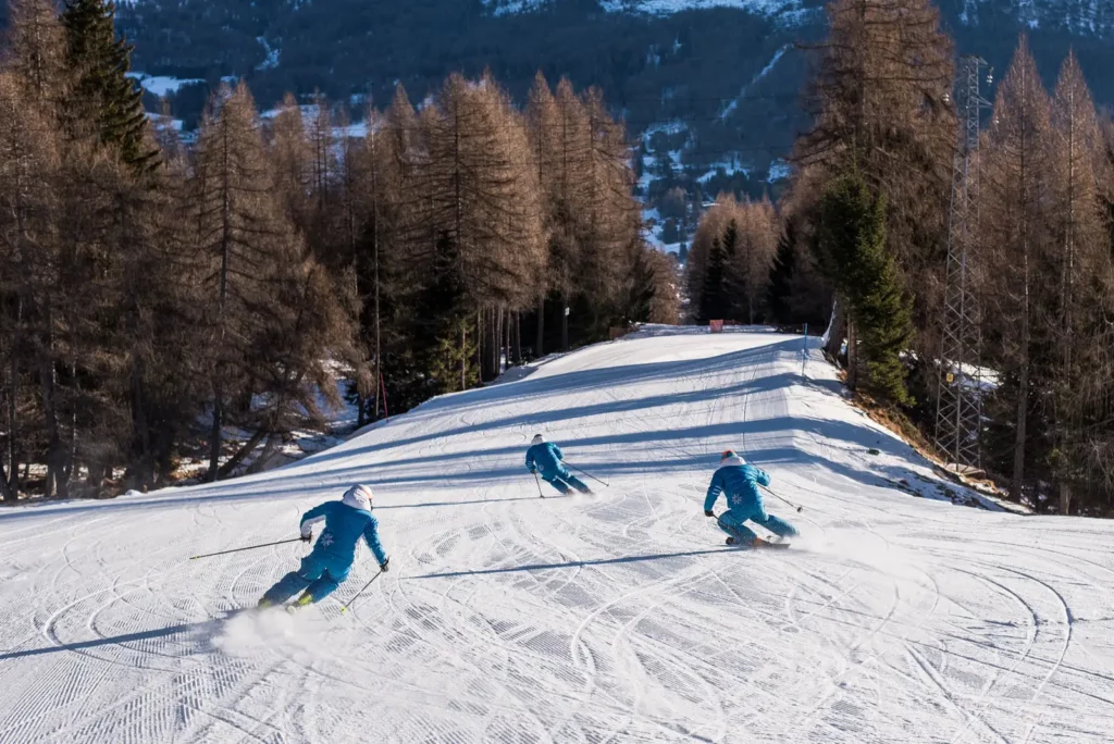 Lezioni di sci a Cortina d’Ampezzo, sciatori in discesa su pista battuta tra boschi innevati e panorama alpino