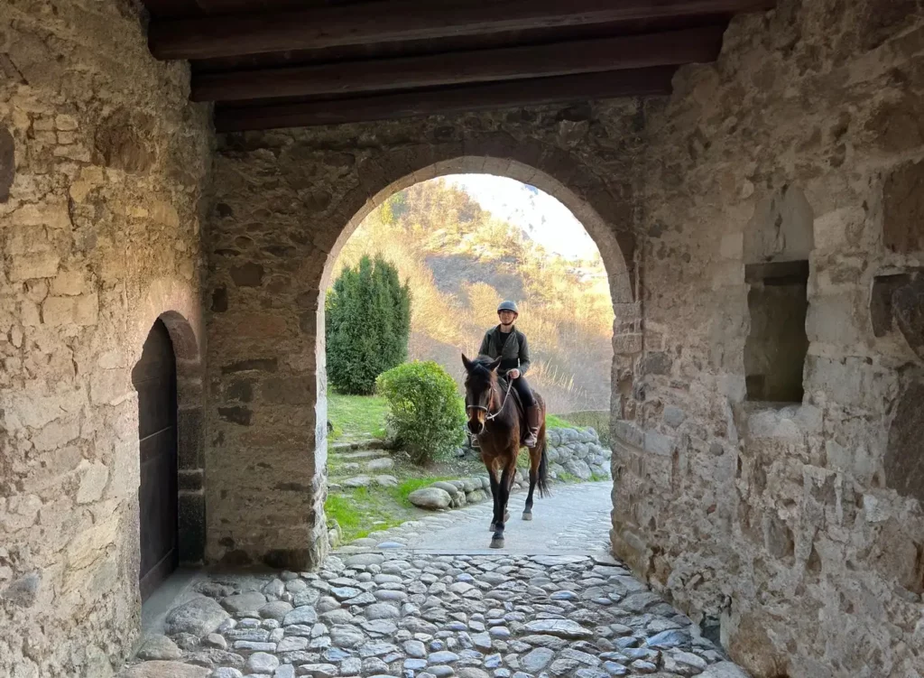 Passeggiata a cavallo in Val Brembana: cavaliere attraversa un arco in pietra con panorama di valle sullo sfondo