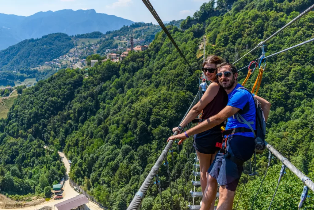 Ponte tibetano in Val Brembana: due persone con imbrago sospese sulla valle boscosa, prima dell’esperienza in grotta