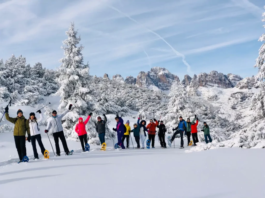 Ciaspolata di gruppo a Canazei nelle Dolomiti, escursione sulla neve con panorama di guglie e boschi innevati