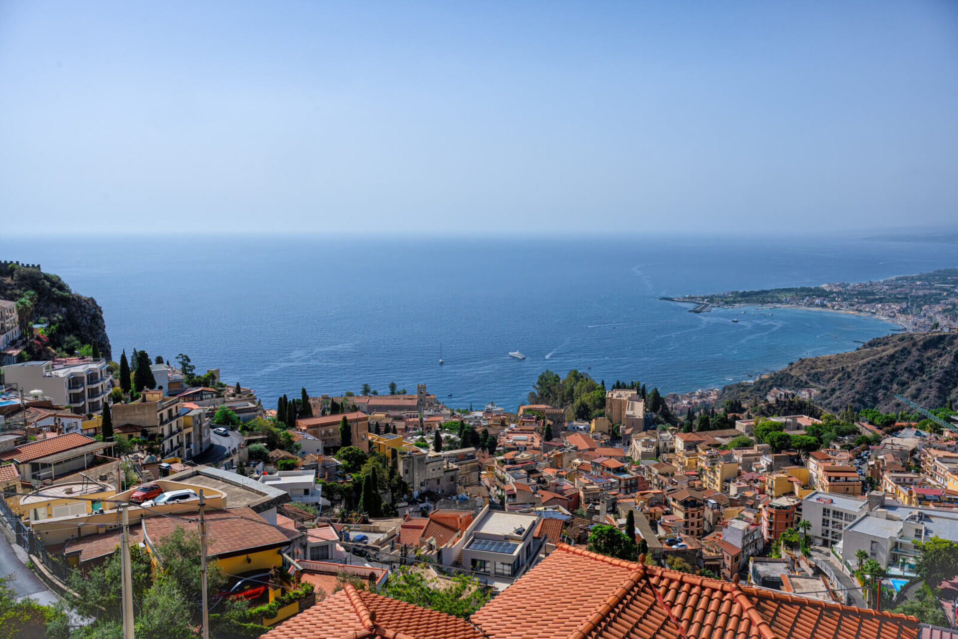 Panorama dall'alto di Taormina con tetti in terracotta e vista sul mare azzurro della Sicilia, ideale per esperienze turistiche e tour panoramici.