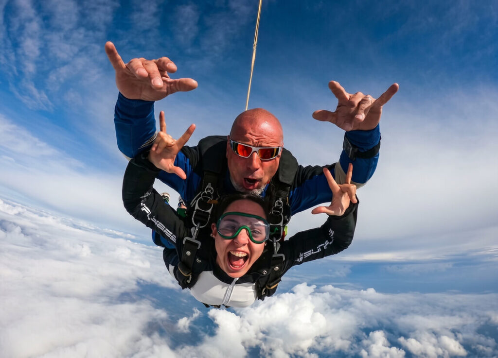 Lancio in paracadute tandem nei cieli di Roma, con un istruttore e una ragazza che sorridono in caduta libera sopra le nuvole.