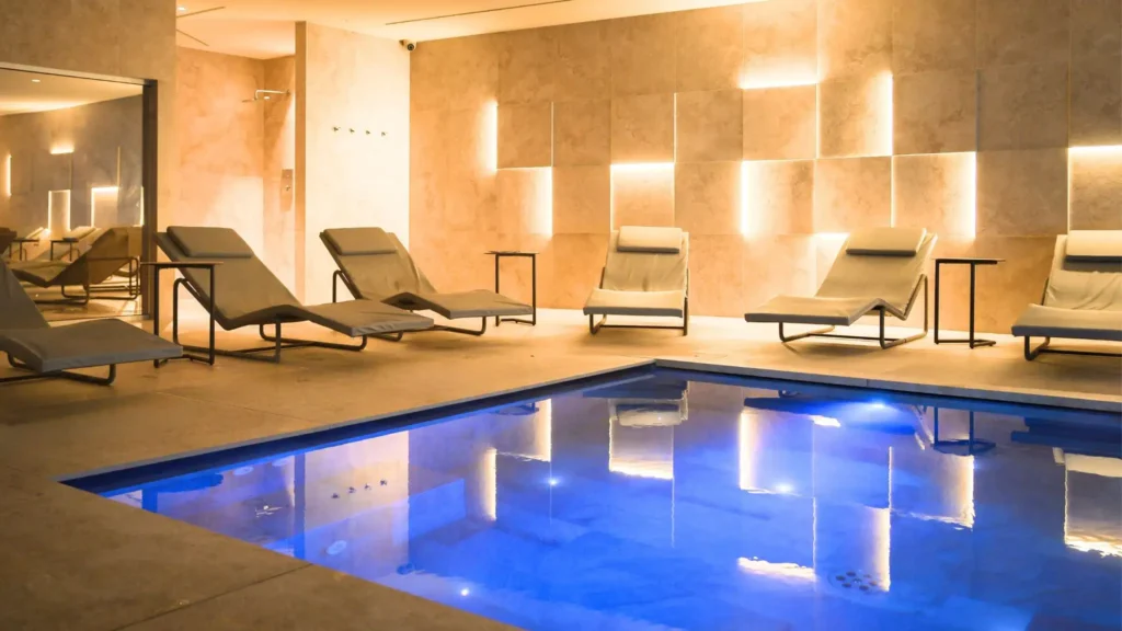 Interno di un moderno centro benessere e spa a Erba, in Lombardia, con una piscina riscaldata illuminata di blu e lettini per il relax.