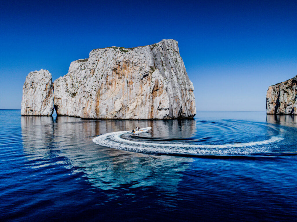 Vista di un gommone in velocità davanti all'imponente Pan di Zucchero a Masua, durante un'escursione in barca nel Sulcis-Iglesiente.