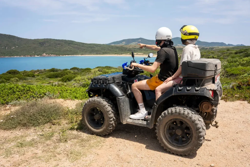 Due persone in quad su un sentiero sterrato con vista sulla spiaggia nella zona di Alghero