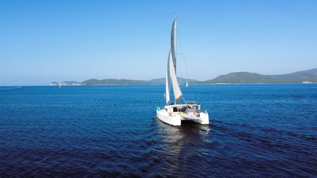 Catamarano a vela nella baia di Alghero con il promontorio di Capo Caccia sullo sfondo