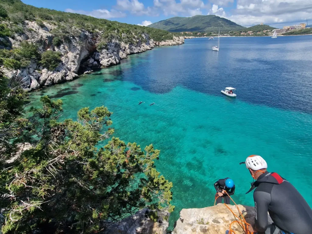 Persona con casco ed equipaggiamento da coasteering affacciata su una caletta turchese a Cala Dragunara