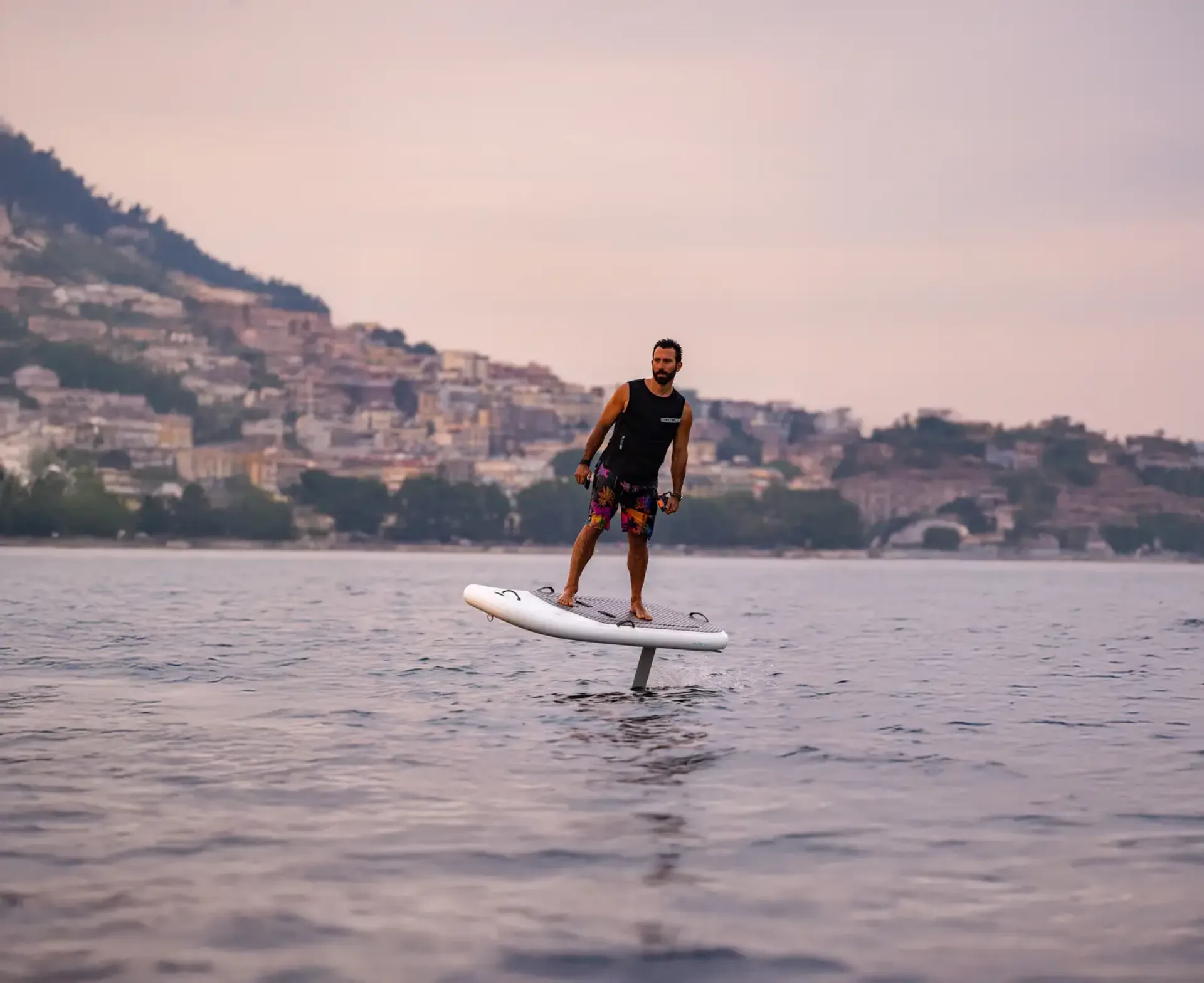 Uomo in piedi su un eFoil che plana sull'acqua al tramonto con costa italiana sullo sfondo