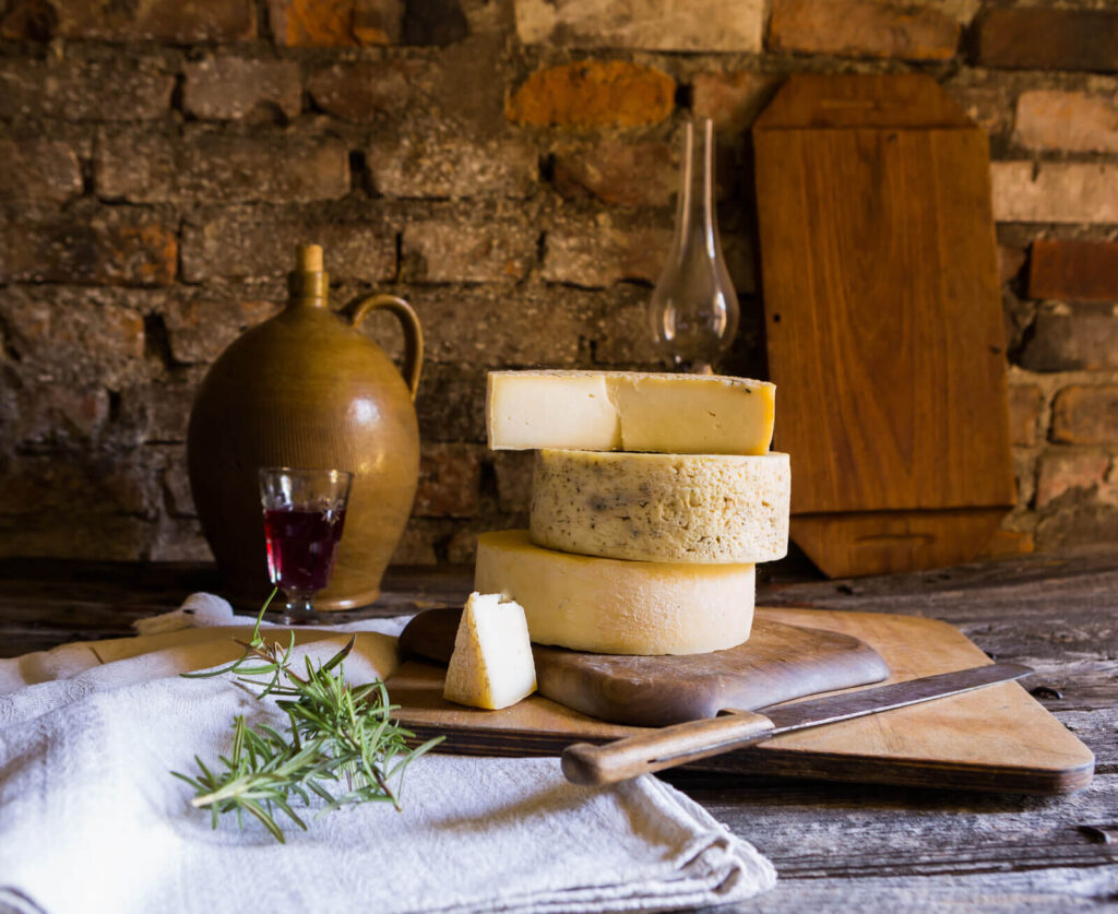 Forme di pecorino sardo stagionato su tagliere rustico con vino rosso, per una degustazione formaggi in Sardegna