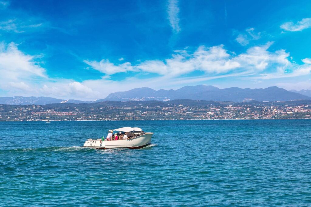 Barca a motore sul Lago di Garda con montagne e cittadina sullo sfondo, escursioni in barca Trentino